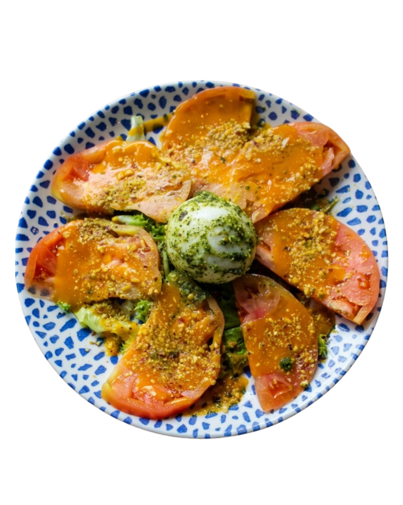 Ensalada de burrata con tomate valenciano, pesto de pistachos, coulis de mango y rúcula.