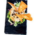 Timbal de ensaladilla rusa con crujientes triángulos de pasta, servido sobre una cama de lechuga.