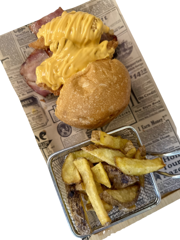 Hamburguesa La T-Rex con carne de chuletón de buey madurado, chili con carne, pollo frito, bacon y cascada de cheddar fundido, acompañada de patatas fritas.