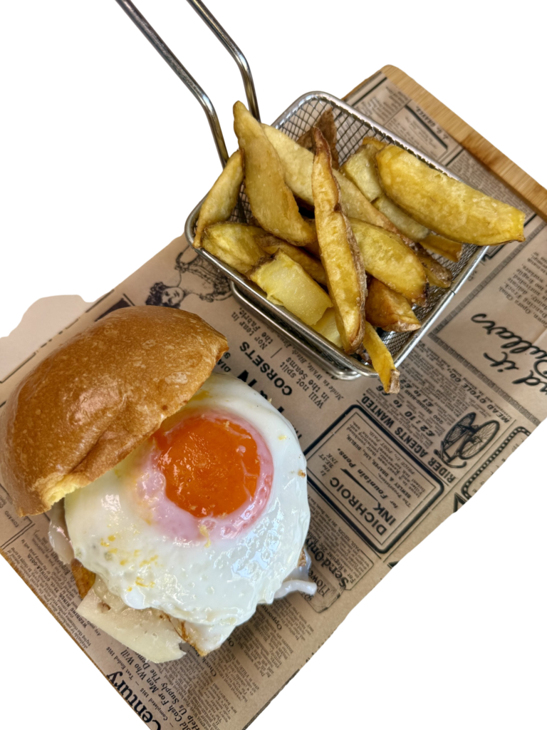 Hamburguesa con carne de chuletón de buey madurado, panceta ibérica, queso manchego, queso edam fundido y huevo, acompañada de patatas fritas.