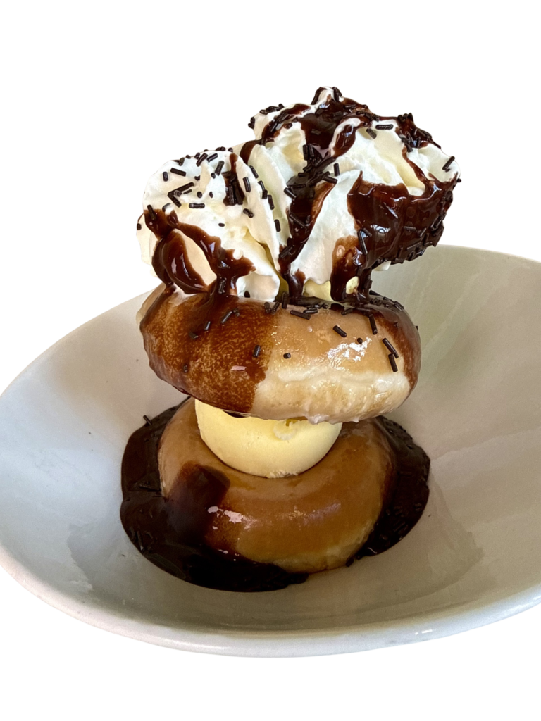 Donut gigante glaseado con dos bolas de helado, chocolate caliente, dulce de leche y nata montada, servido en un plato.